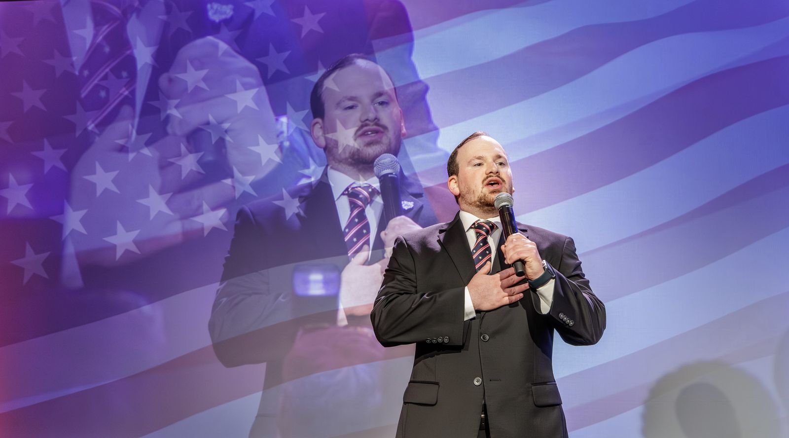 Speaker on stage with American flag video overlay